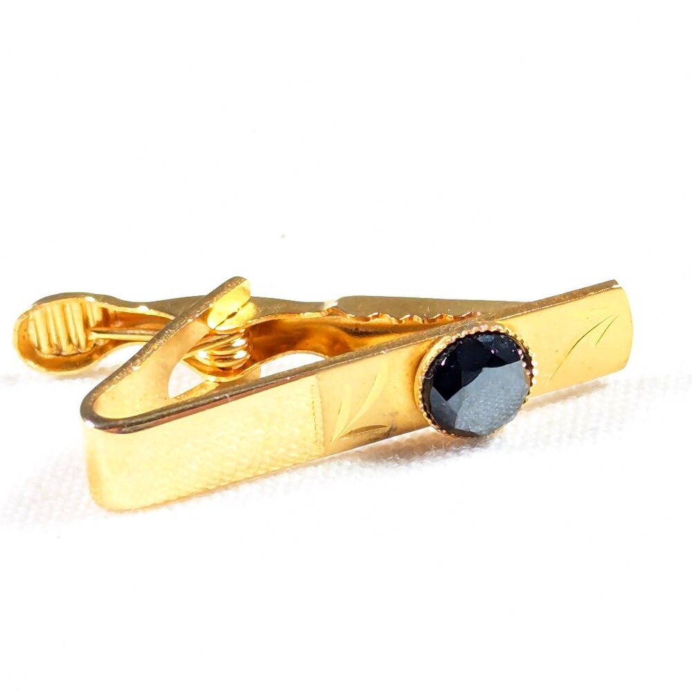 Small tie clip in gold tone with inset blue or black stone